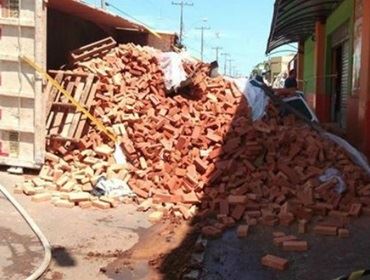 Caminhão carregado com tijolos tomba sobre carro que 'desaparece'